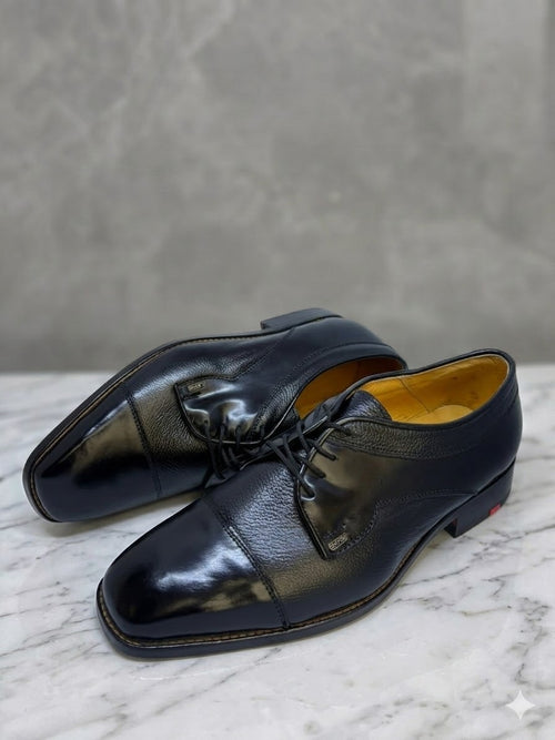 Pair of black dress shoes on a marble surface with a gray background